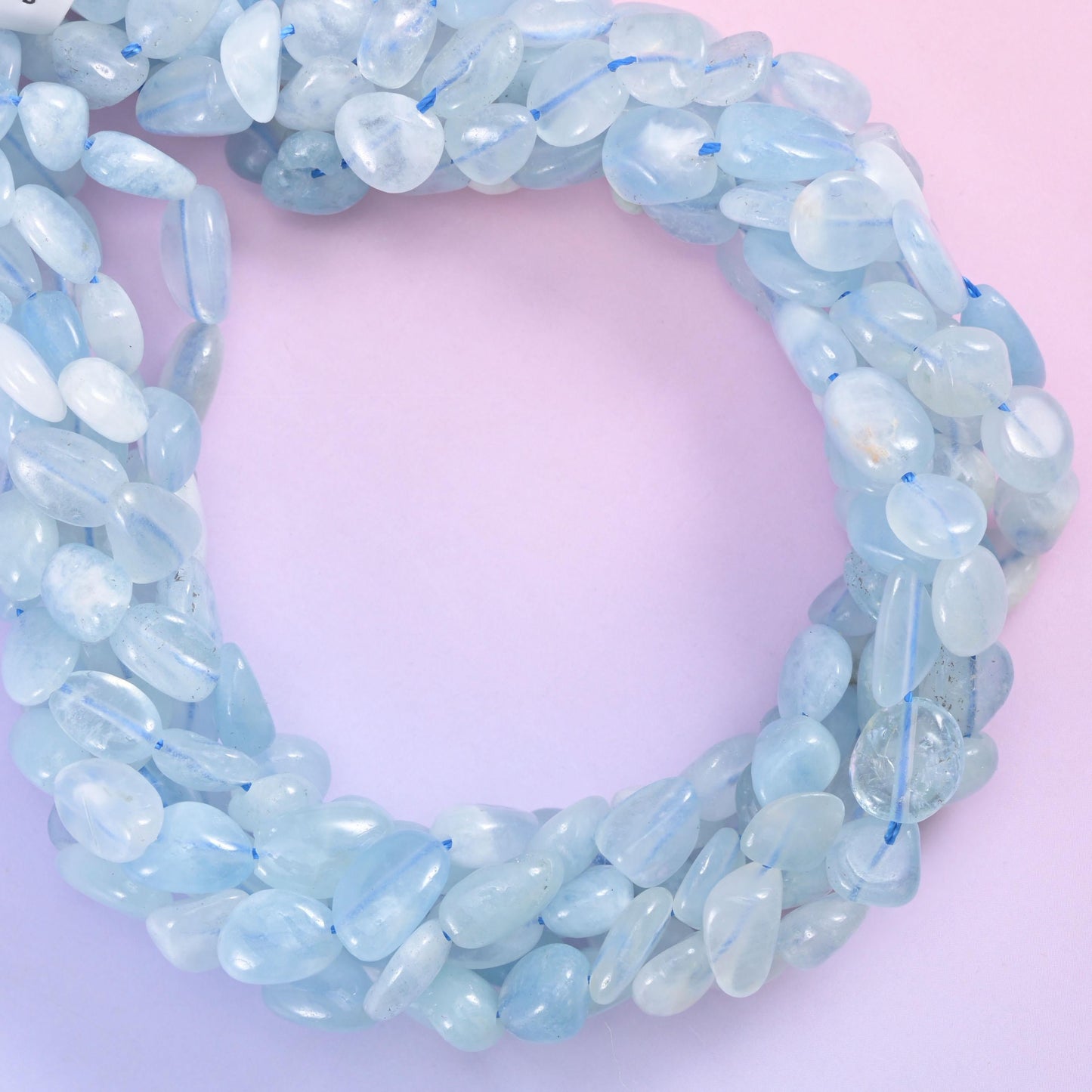 Aquamarine nugget strand coiled into a ring on a pastel pink and purple backdrop