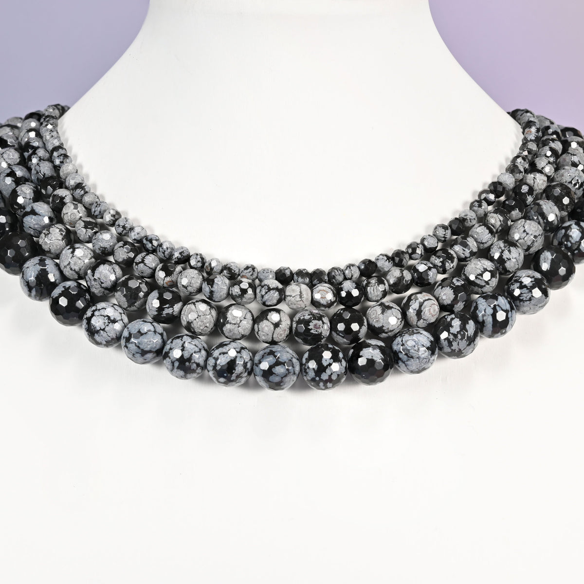 Snowflake Jasper faceted round bead strands in graduating sizes displayed around a white necklace bust against a lavender background.