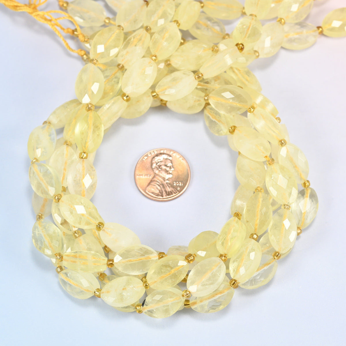 Citrine faceted flat oval beads 9x14mm coiled in a loop around a US penny for scale, close-up of the faceted flat oval shape