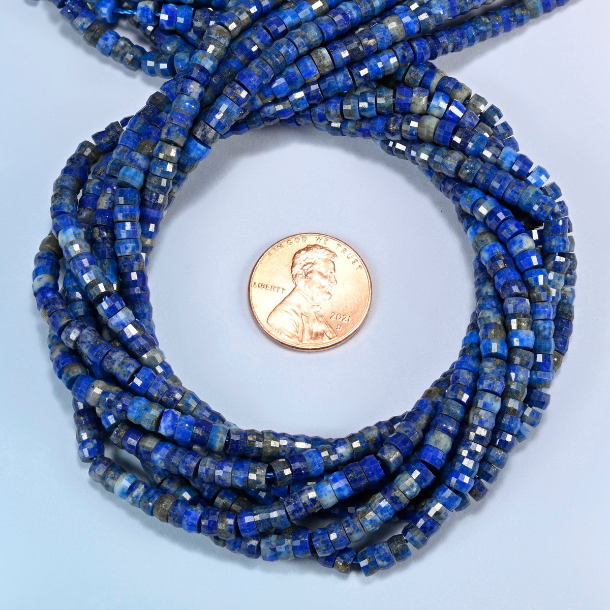 Lapis faceted heishi disc beads 2x4mm coiled in a loop around a US penny for scale, close-up of the faceted disc shape