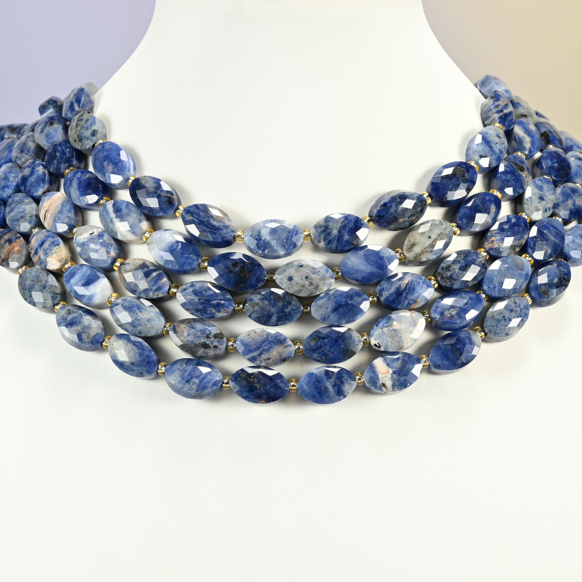 Orange sodalite faceted flat oval strands arranged as a layered collar on a white display bust, blue and peach beads across the neck