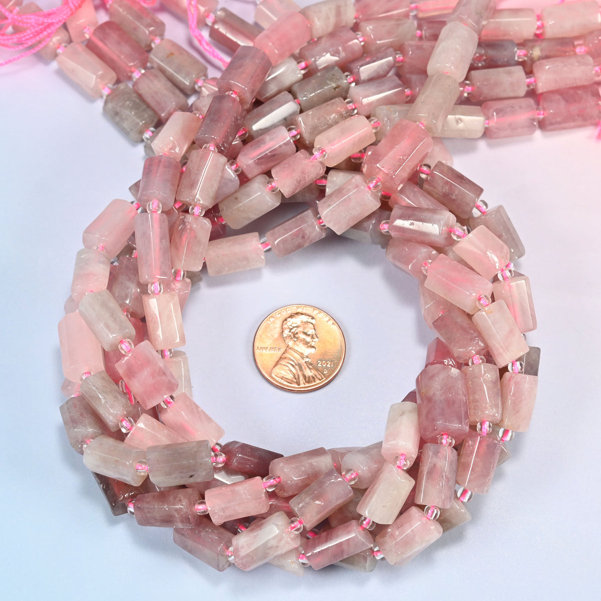 Madagascar multi color rose quartz faceted tube beads wound in a ring around a US penny, close view of the tube cut.