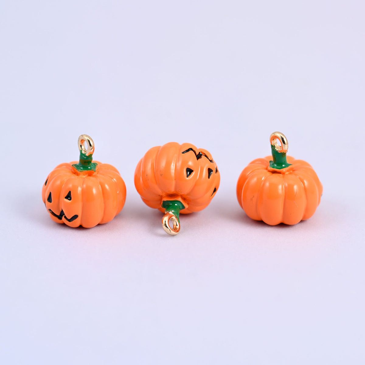 Three enamel pumpkin charms in a row, showing the jack o lantern face and the plain back of the same charm.