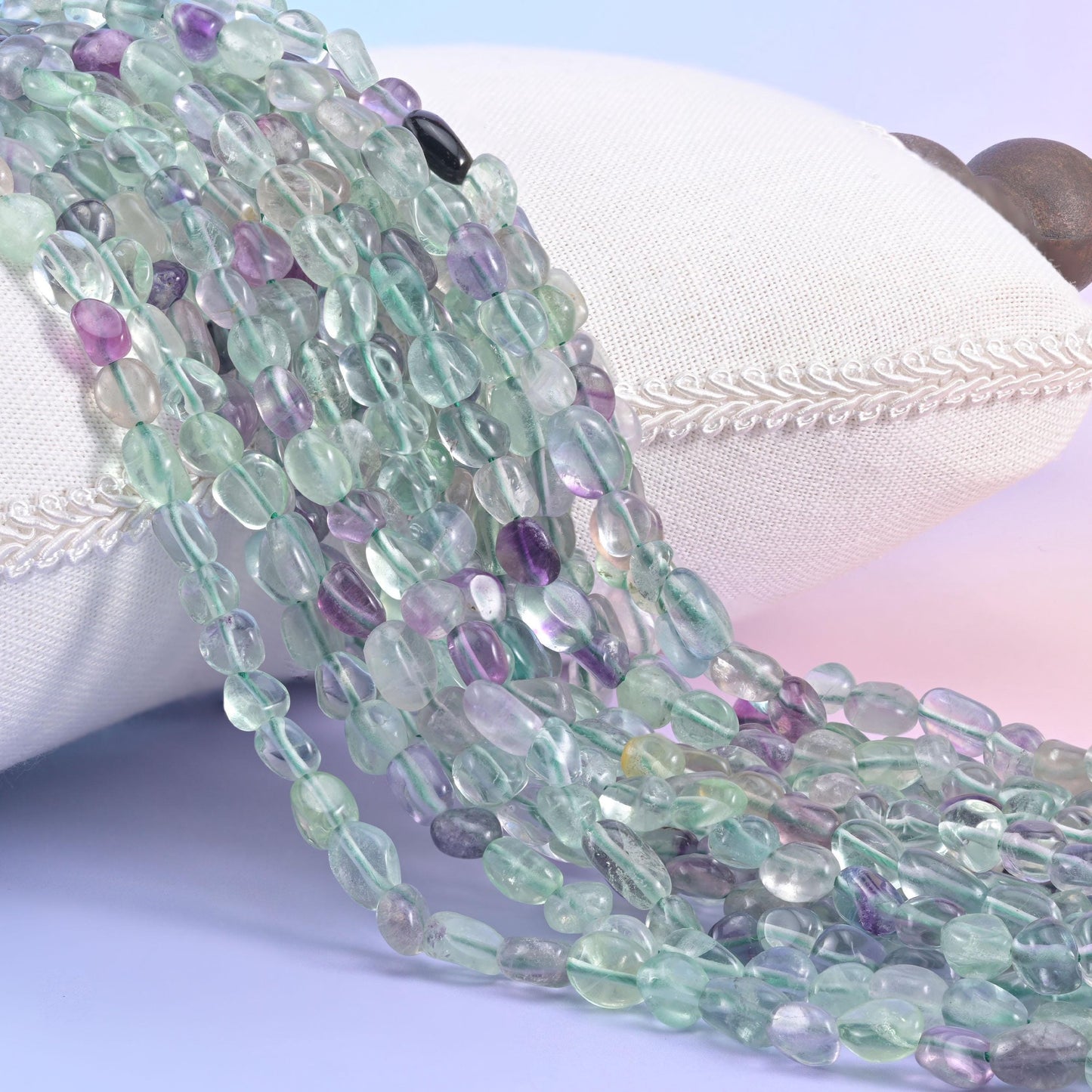 Mint green and purple fluorite nugget strands spilling over a white cushion