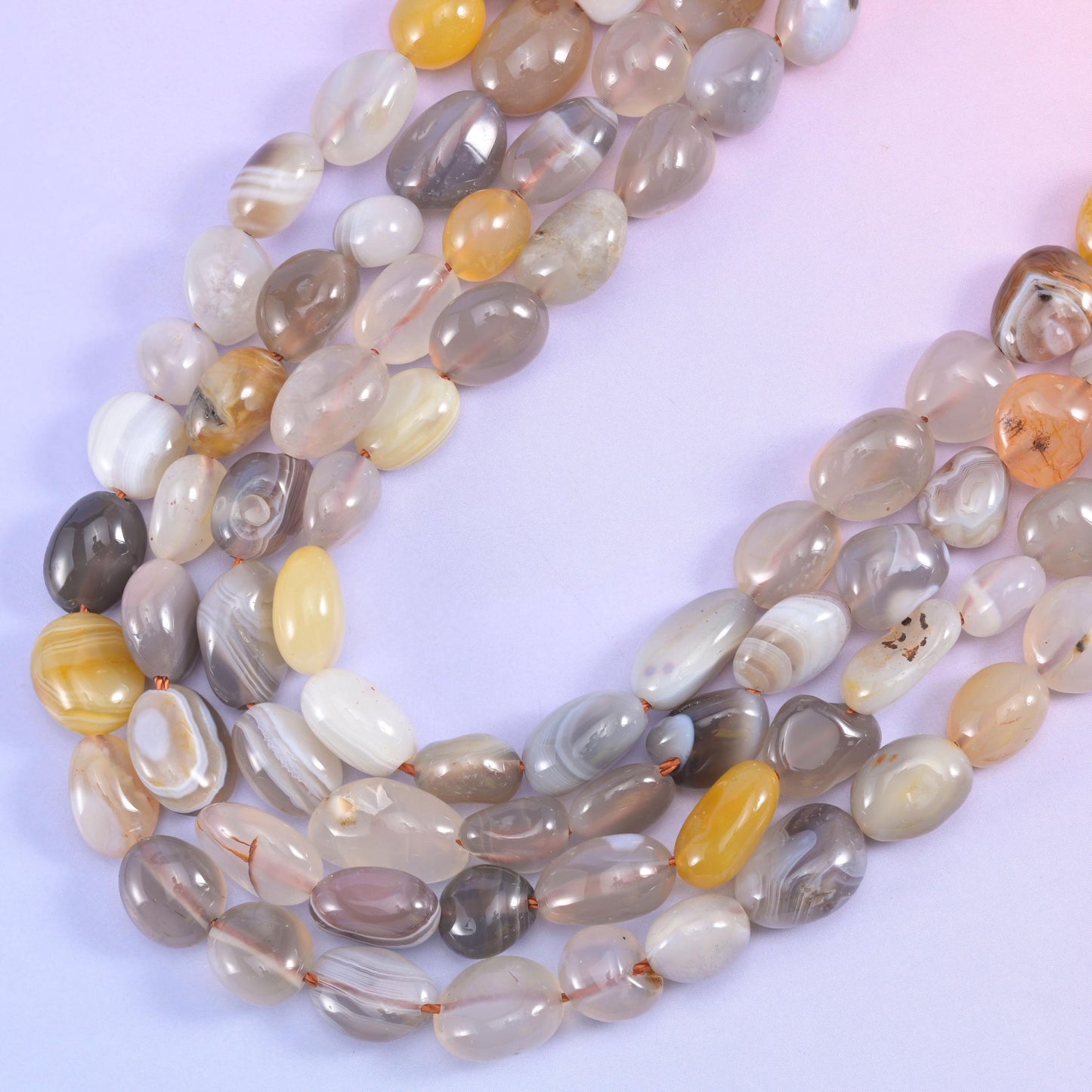 Botswana Agate nugget strands curving in a U against a pale backdrop