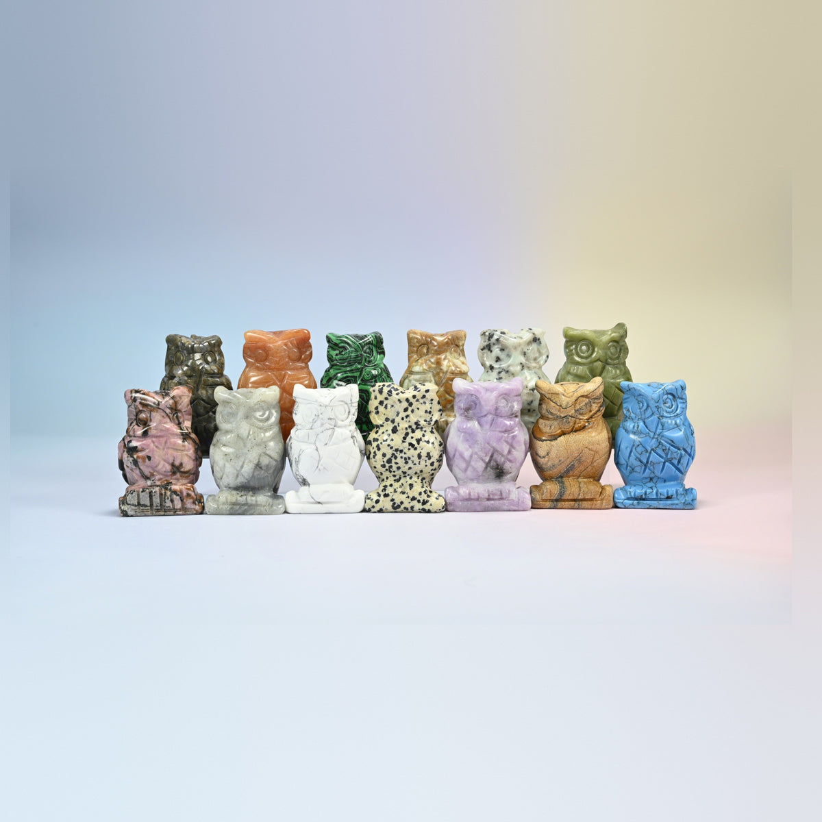 Row of owl crystal carvings in lepidolite, dalmatian jasper, white howlite, picture jasper, dyed blue howlite and more