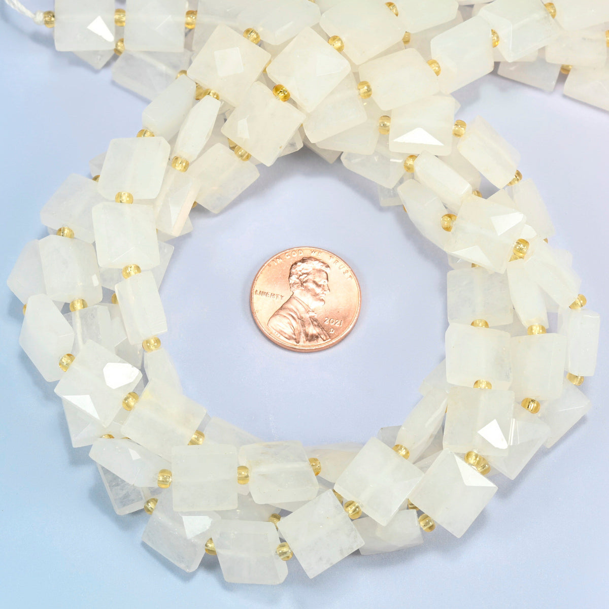 Clear quartz faceted flat square beads 10x10mm coiled in a loop around a US penny for scale, close-up of the faceted flat square shape