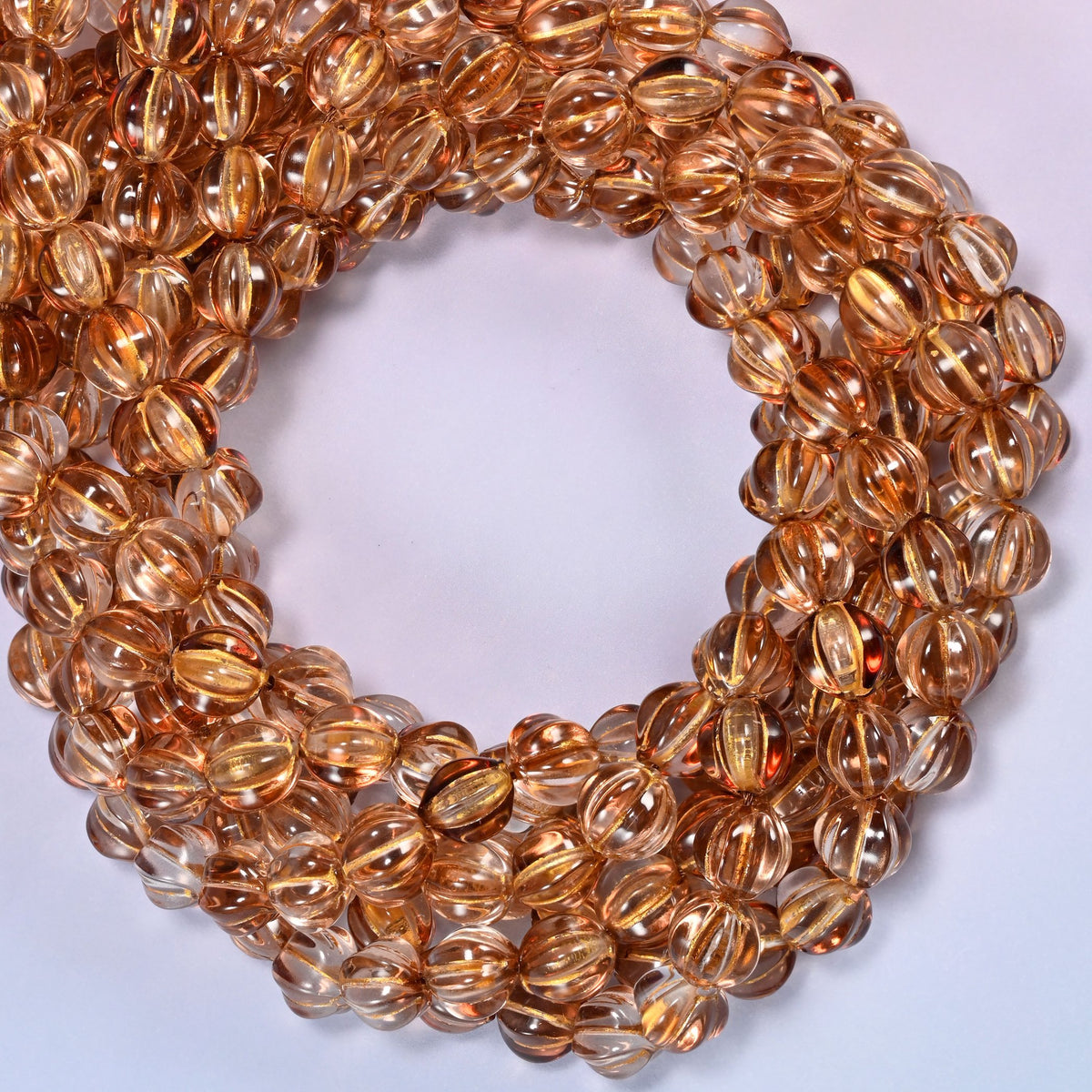 Brown pumpkin glass beads coiled with the open center to one side, showing the fluted grooves end on.