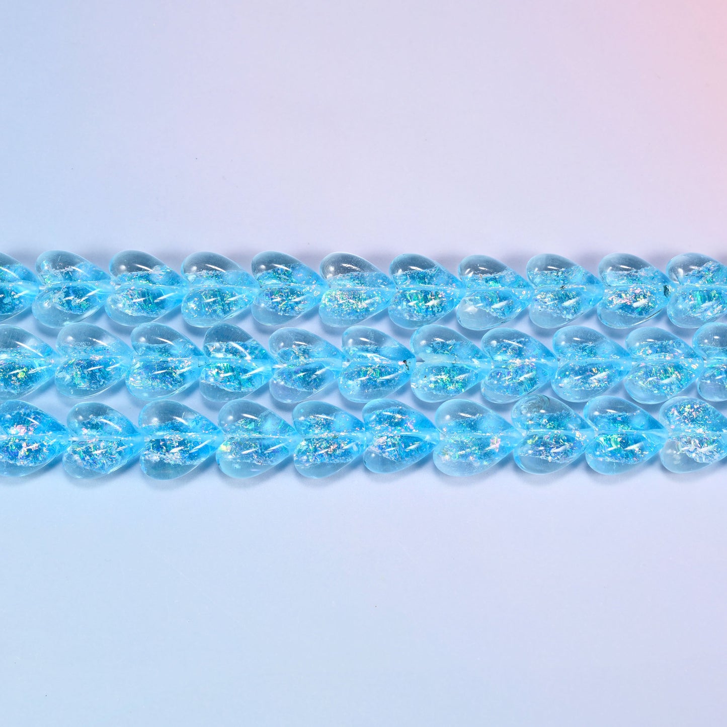 Iridescent light blue heart glass beads seen side on, showing the 8.54mm puffed thickness of each heart