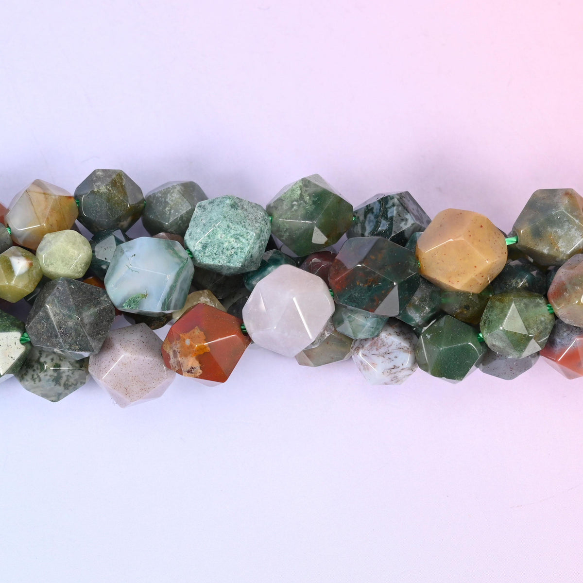 Indian Agate faceted beads close up in a single row, flat triangular star cut planes over green, red and amber layers