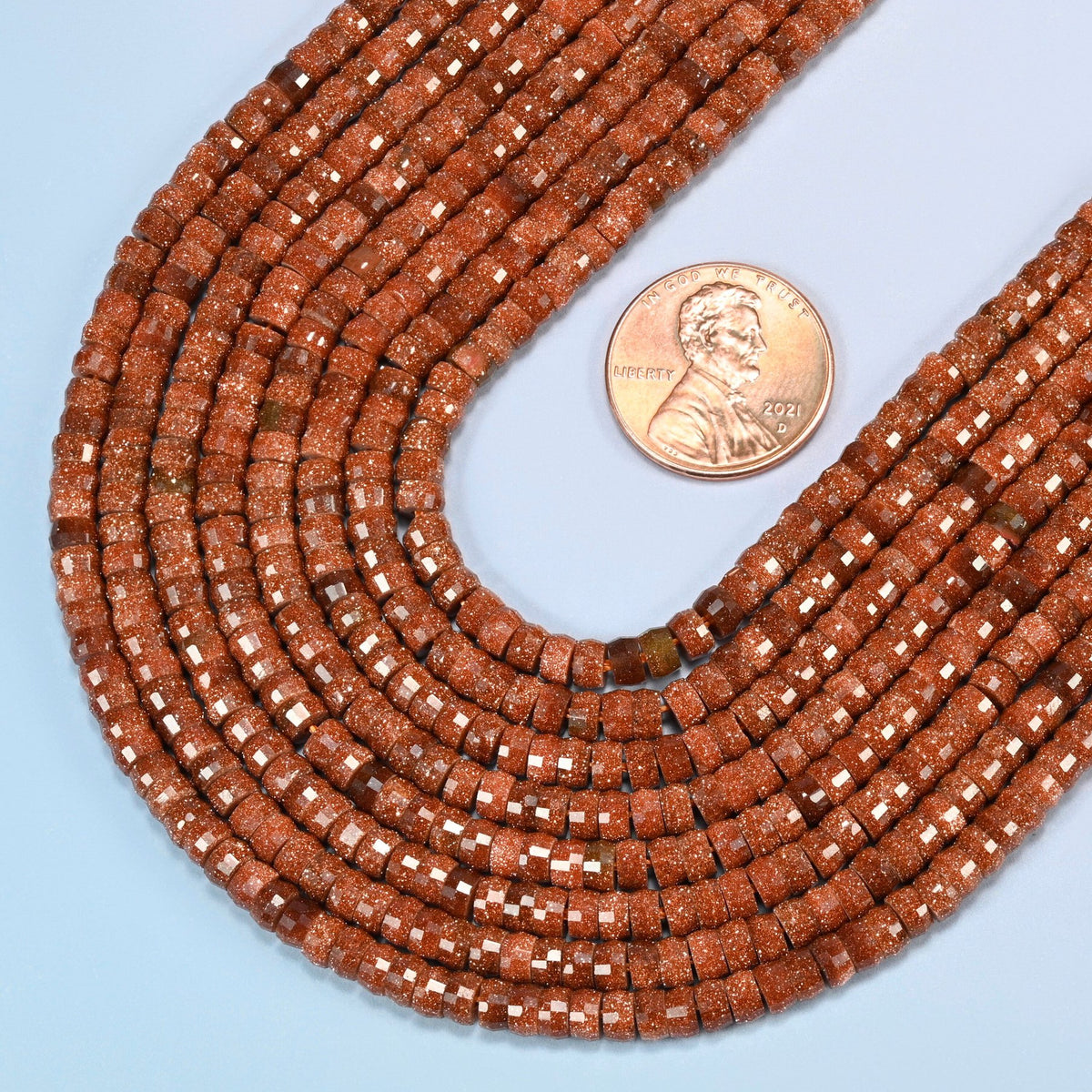Close view of gold sandstone faceted heishi disc strands curving beside a US penny for scale