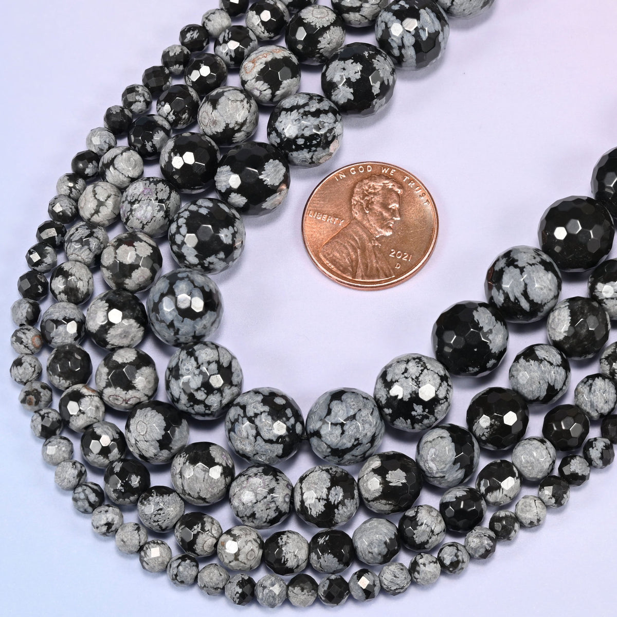 Snowflake Jasper faceted round beads coiled into a teardrop-shaped loop with a penny resting inside the loop for size reference.