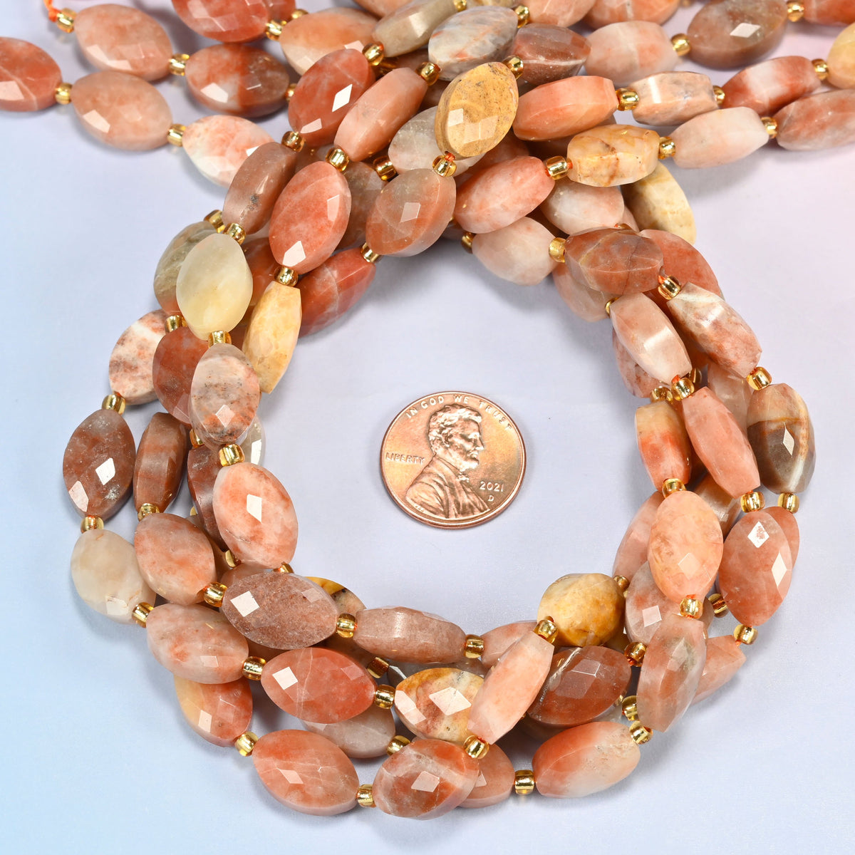 Red crazy agate faceted flat oval beads 9x14mm coiled in a loop around a US penny for scale, close-up of the faceted flat oval shape