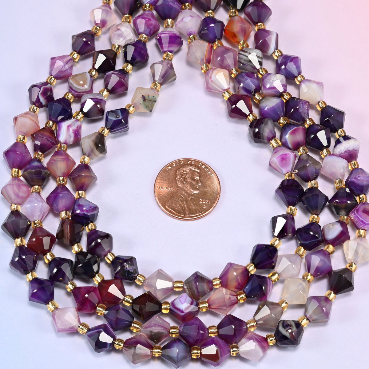 Close-up of 8mm Dyed Purple Strip Agate faceted bicone beads coiled into a circle, highlighting the varied purple tones and banded pattern.