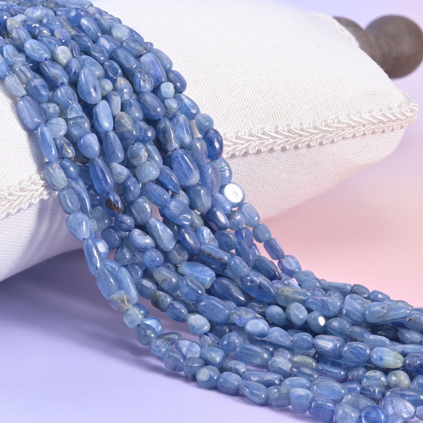 Blue kyanite nugget strands draped over a cream cushion, denim-toned pebbles with silvery streaks