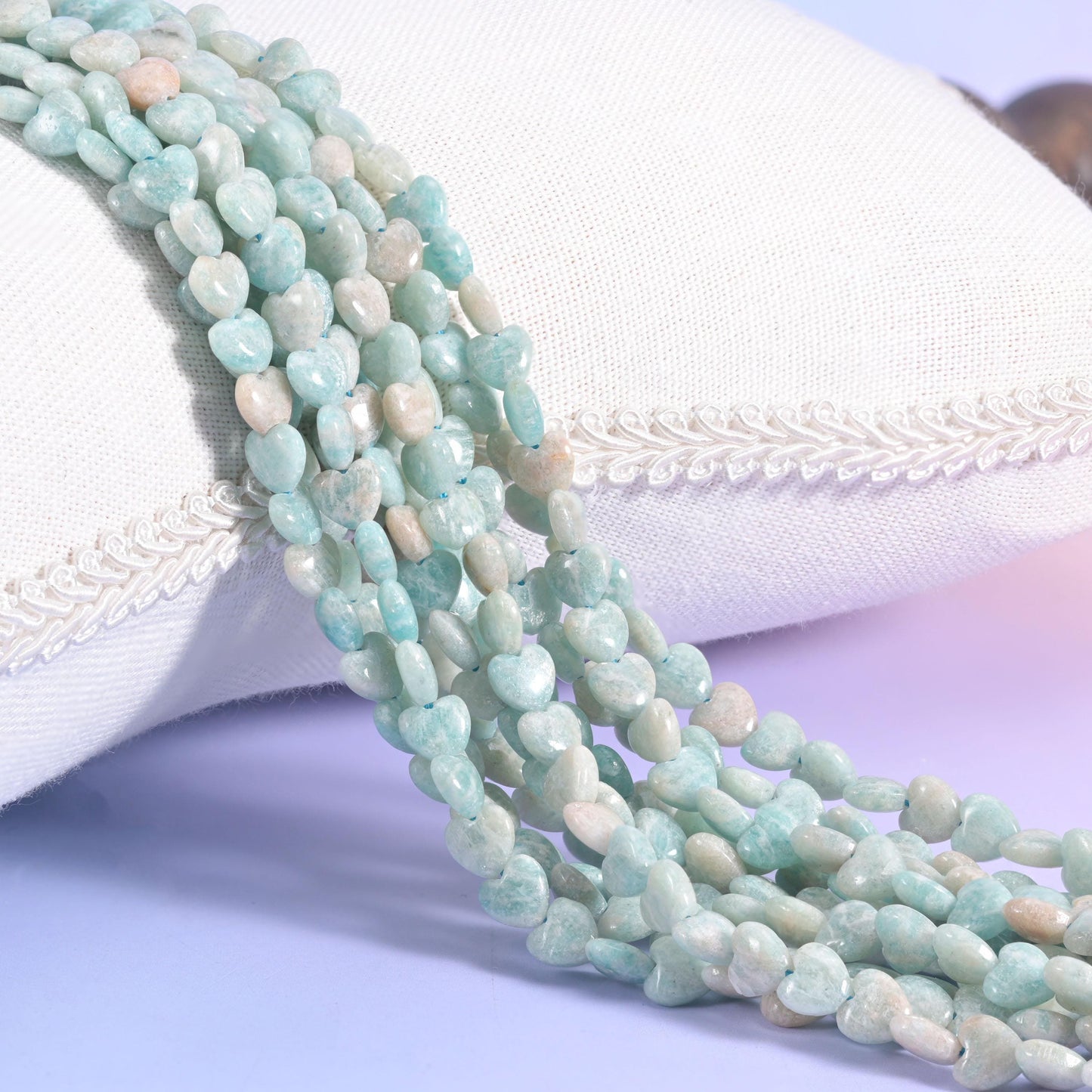 Pale aqua Blue Amazonite heart bead strands leaning against a white cushion
