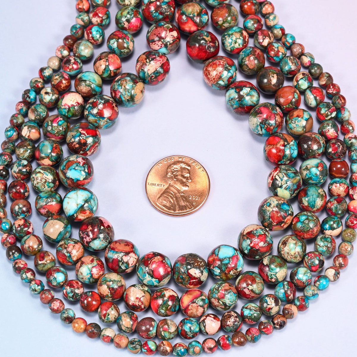Red sea sediment jasper smooth round beads coiled flat into several rings, shown with a US penny in the open center for scale.