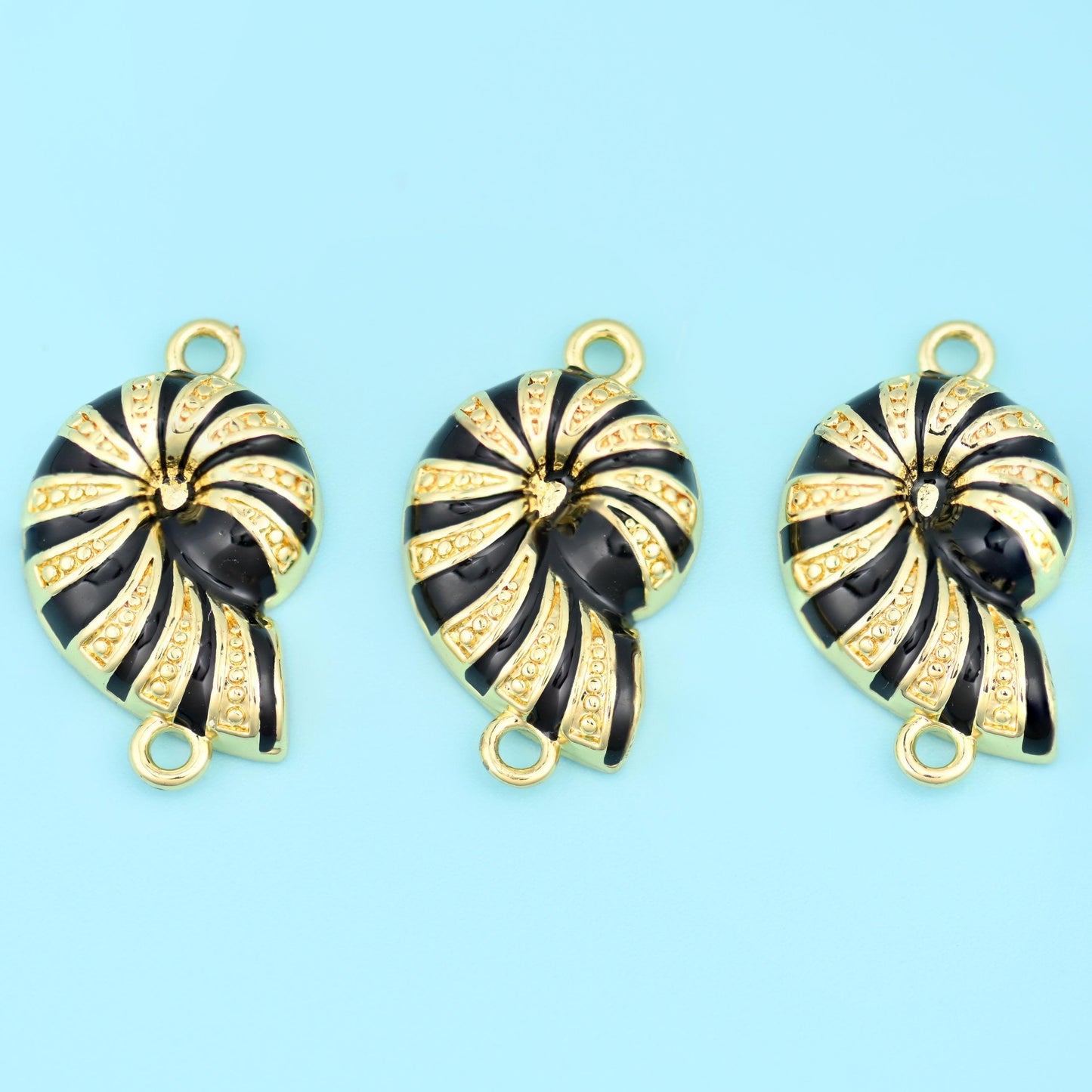 A spiral sea snail shell with glossy black enamel stripes swept between fine textured gold ridges, finished in smooth…
