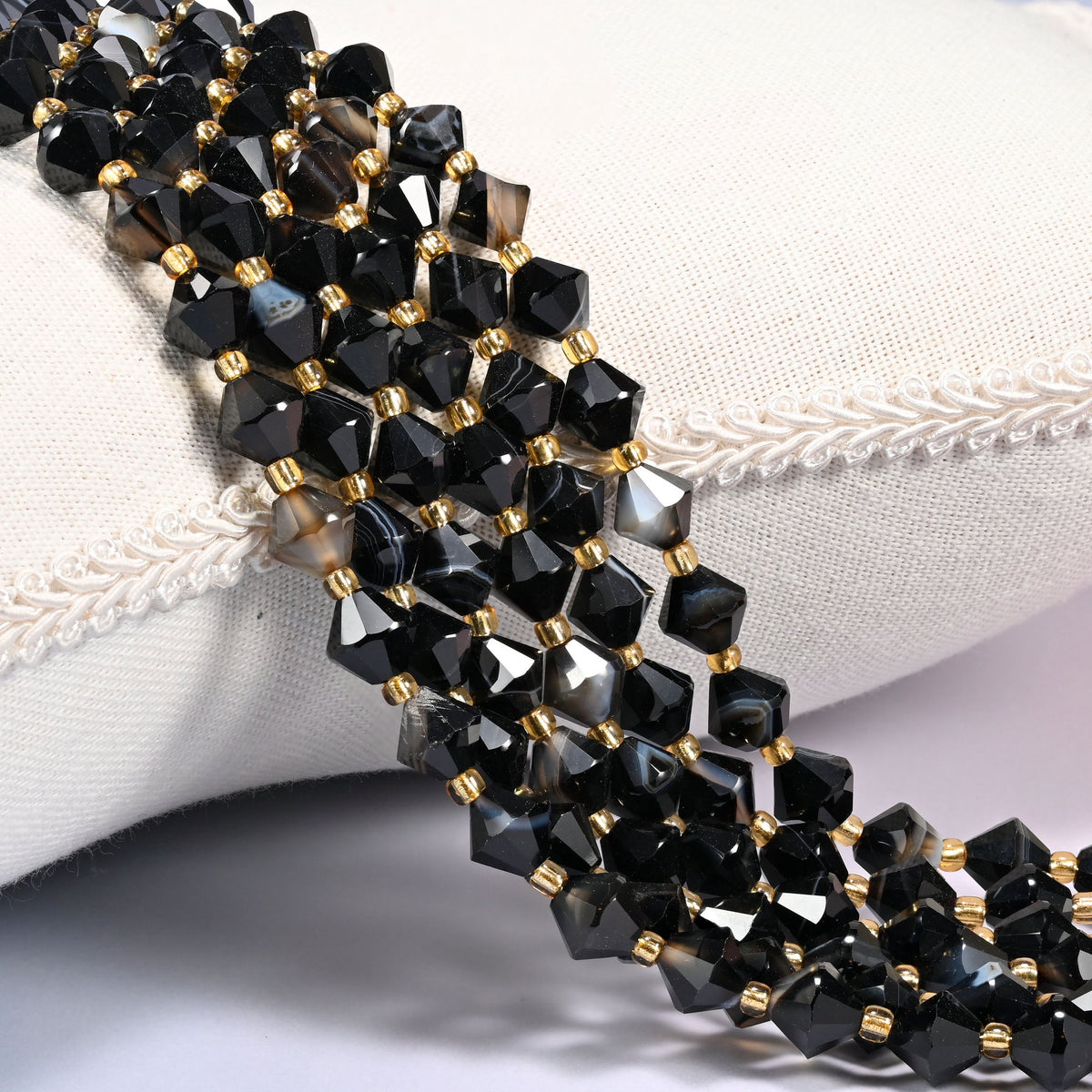 Dyed black strip agate bicone beads laid out on the diagonal in several rows, glossy black with the agate's natural banding still showing, a gold-tone spacer between every bead.