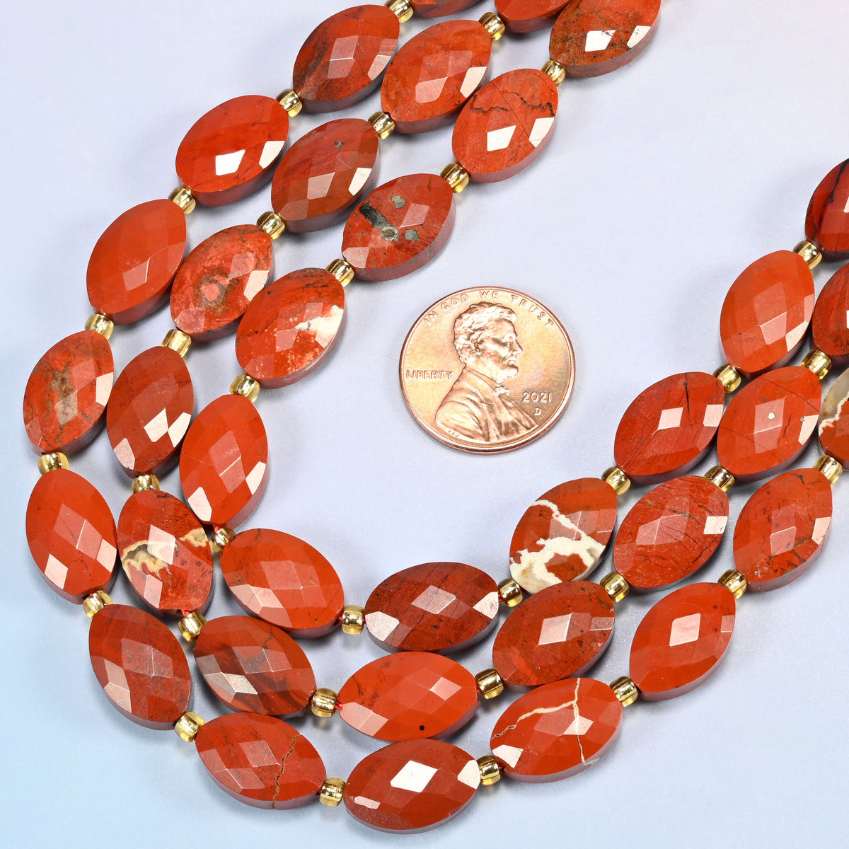 Close view of flower red jasper faceted flat oval strands curving beside a US penny for scale
