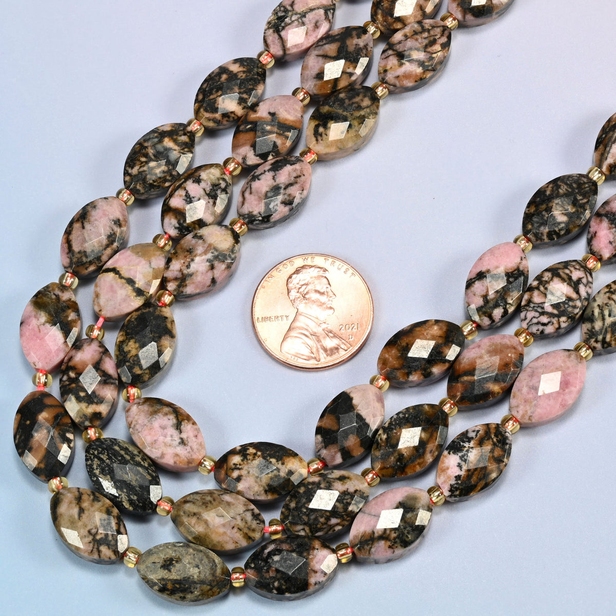 Close view of rhodonite faceted flat oval strands curving beside a US penny for scale