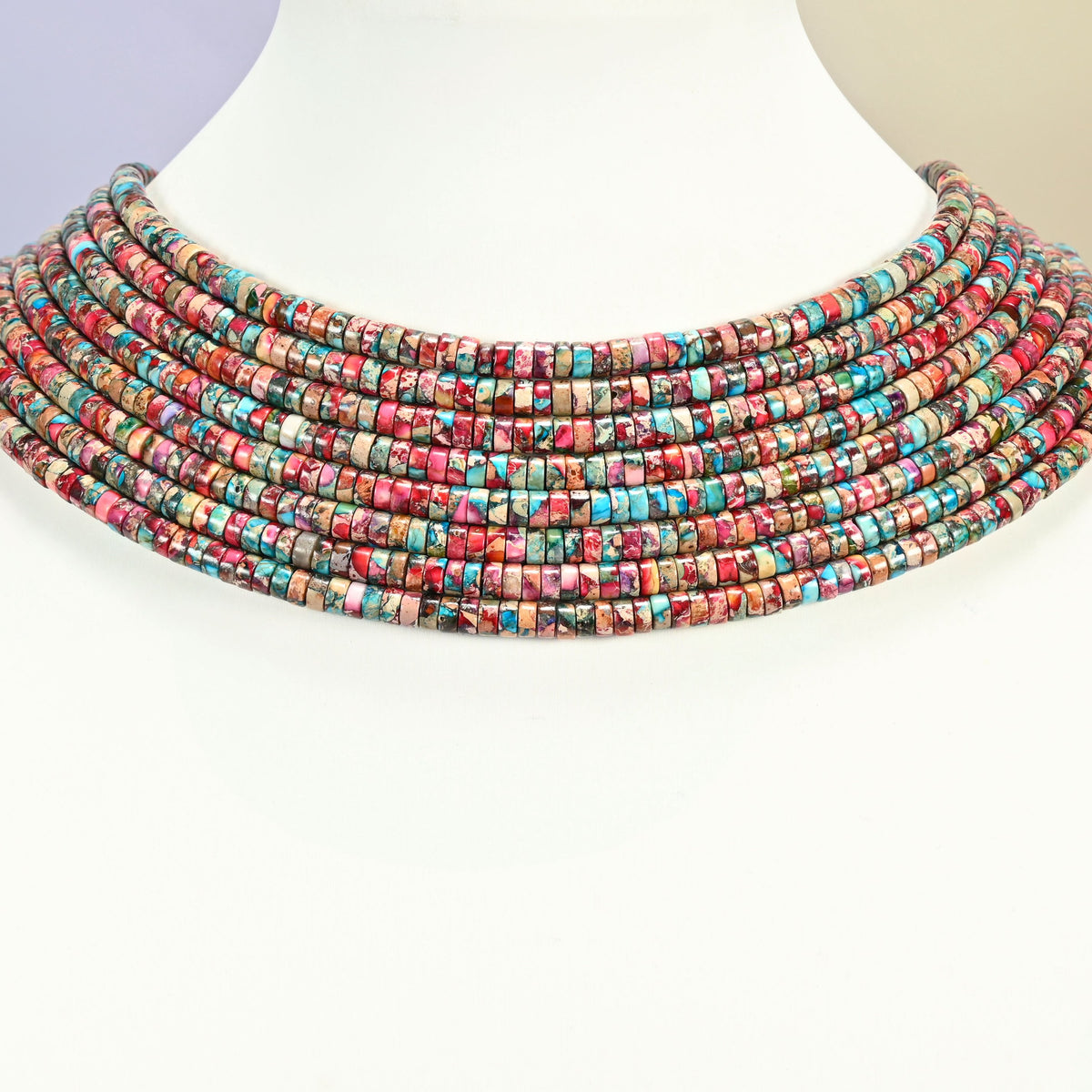 Dyed pink blue sea sediment jasper heishi disc strands arranged as a layered collar on a white display bust