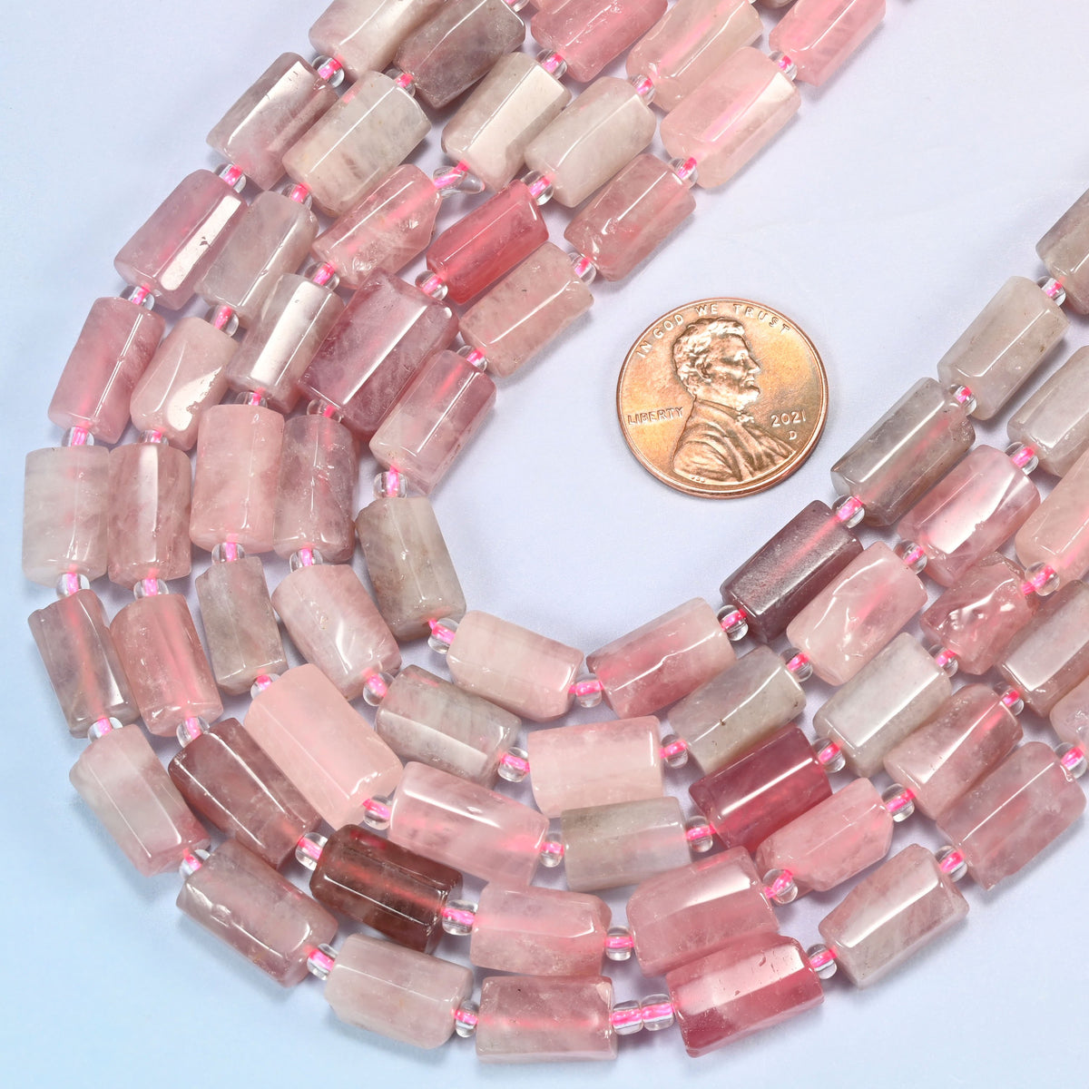 Madagascar multi color rose quartz faceted tube beads coiled in a loop beside a US penny set at the right for scale.