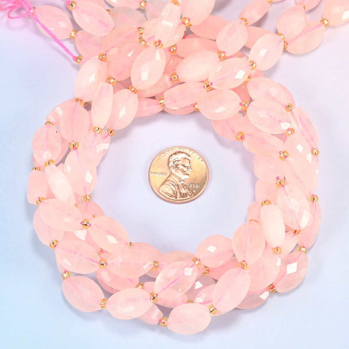 Rose quartz faceted flat oval beads 9x14mm coiled in a loop around a US penny for scale, close-up of the faceted flat oval shape