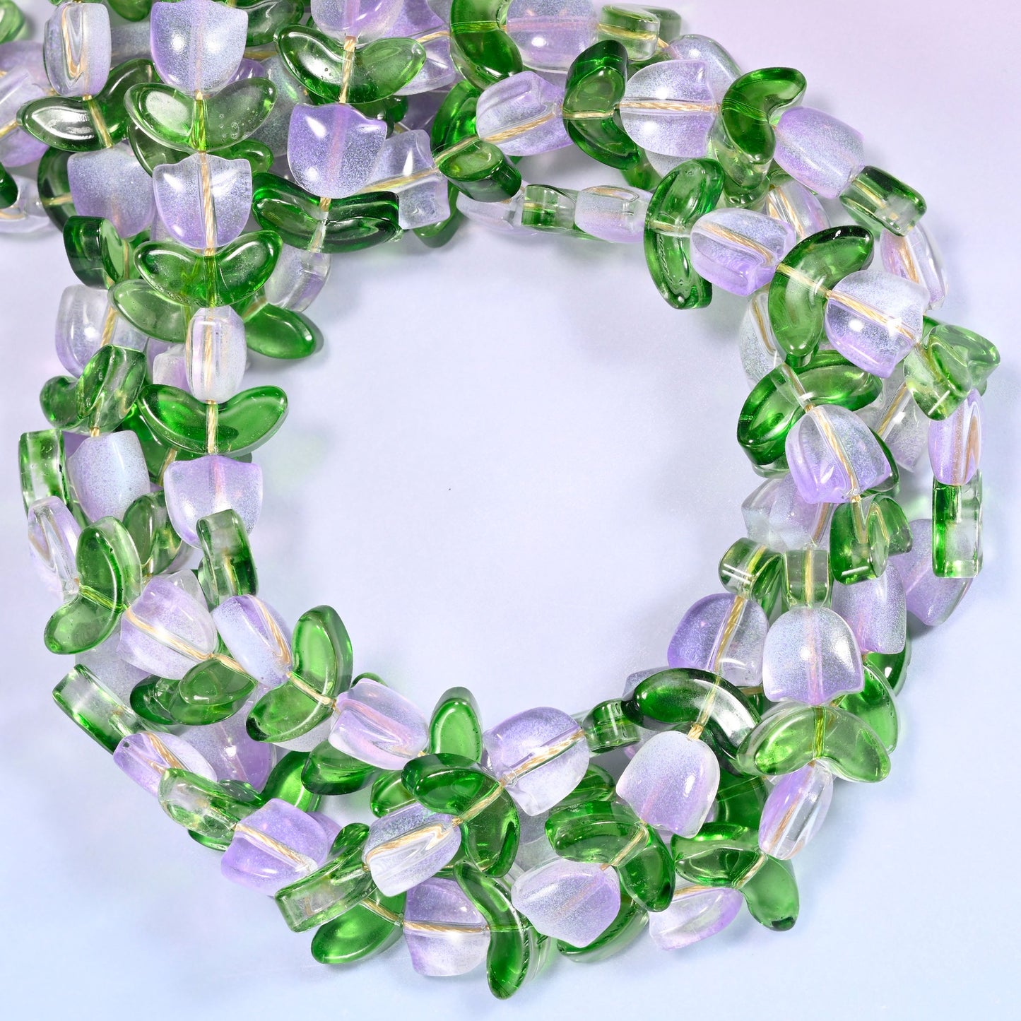 Horizontal row of lavender tulip and green leaf glass beads laid straight across a lavender background, showing the alternating flower and leaf pattern.