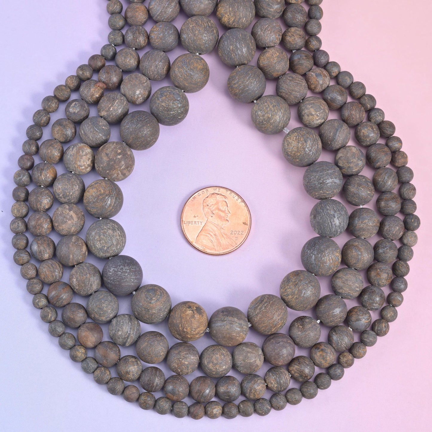 Coiled bronzite strands framing a penny, showing how the 4mm beads compare to the 10mm ones