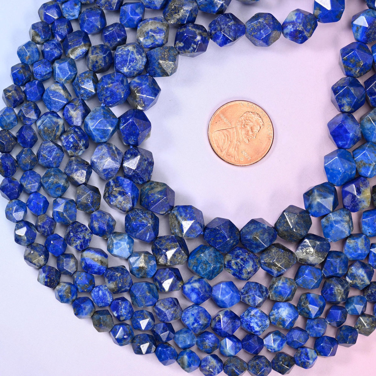Blue Lapis Lazuli diamond star cut beads coiled around a US penny for size reference, centre drilled with a polished faceted finish