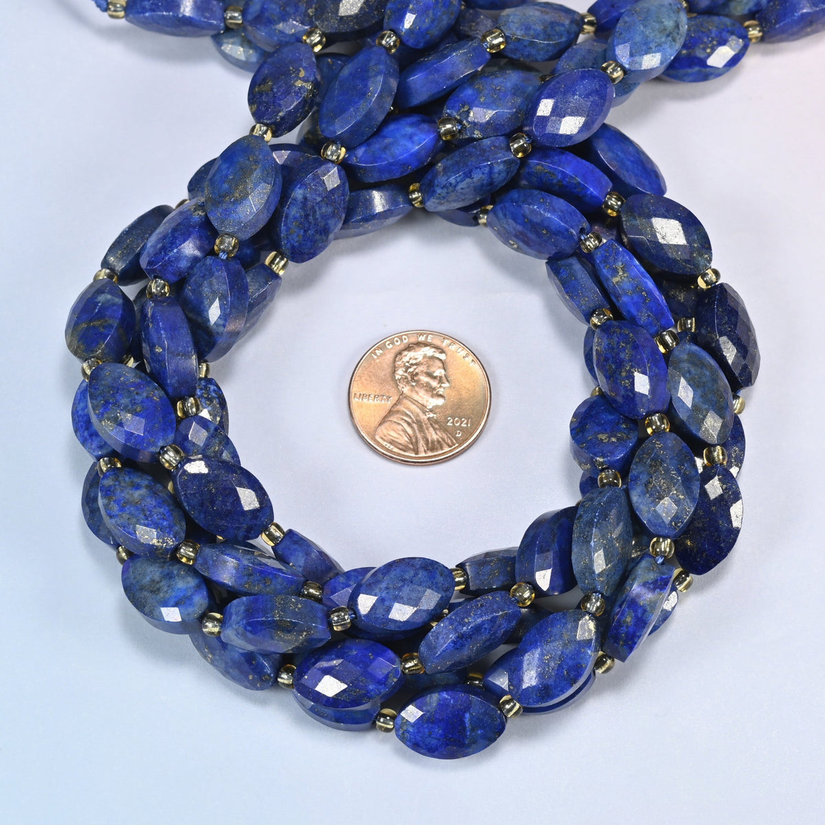 Lapis lazuli faceted flat oval beads 9x14mm coiled in a loop around a US penny for scale, close-up of the faceted flat oval shape