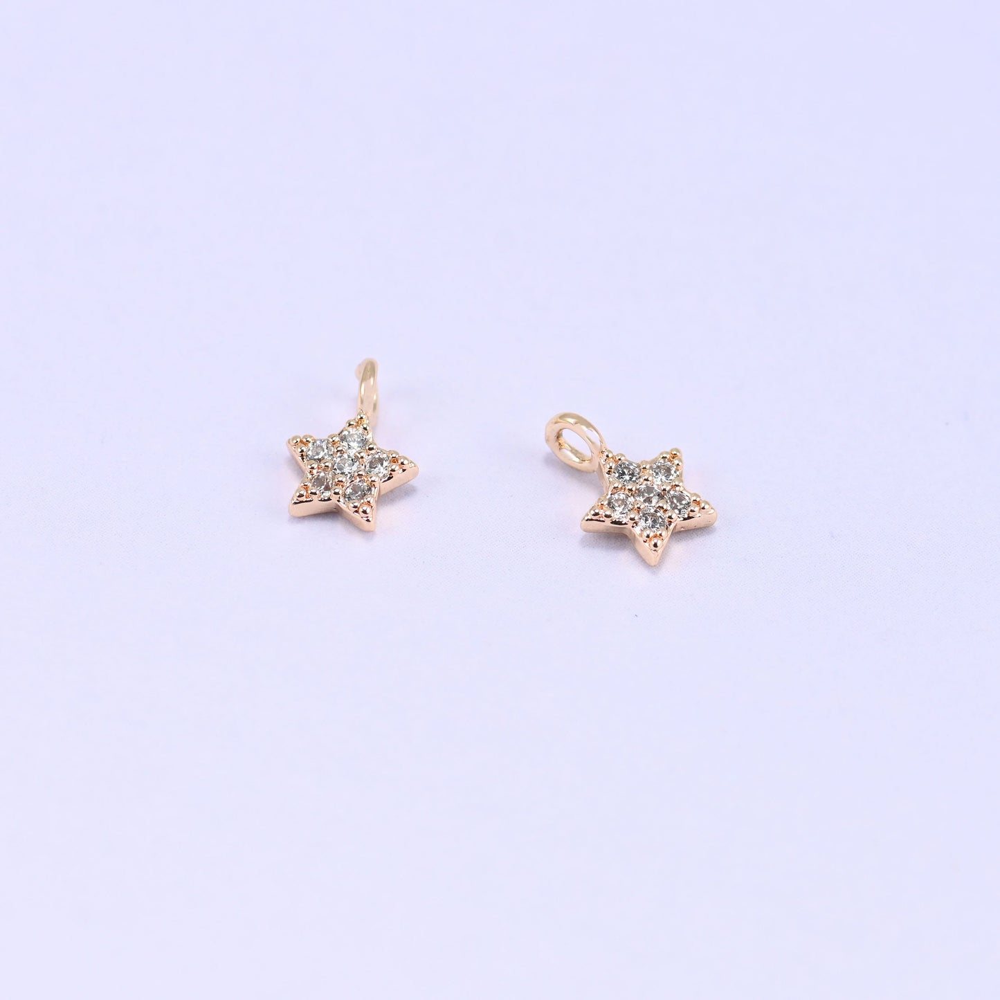 Small gold charms, two star charms with clear cubic zirconia shown close up