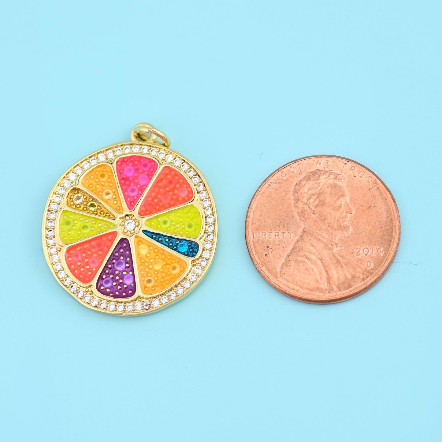 A large fruit slice divided into six glittery enamel wedges in orange, pink, lime, purple and blue, edged all the way round…