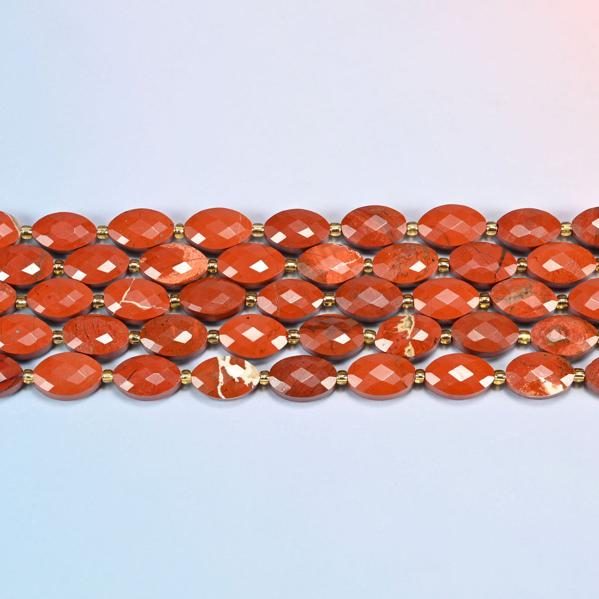 Several strands of flower red jasper faceted flat oval beads laid in straight rows with gold seed bead spacers