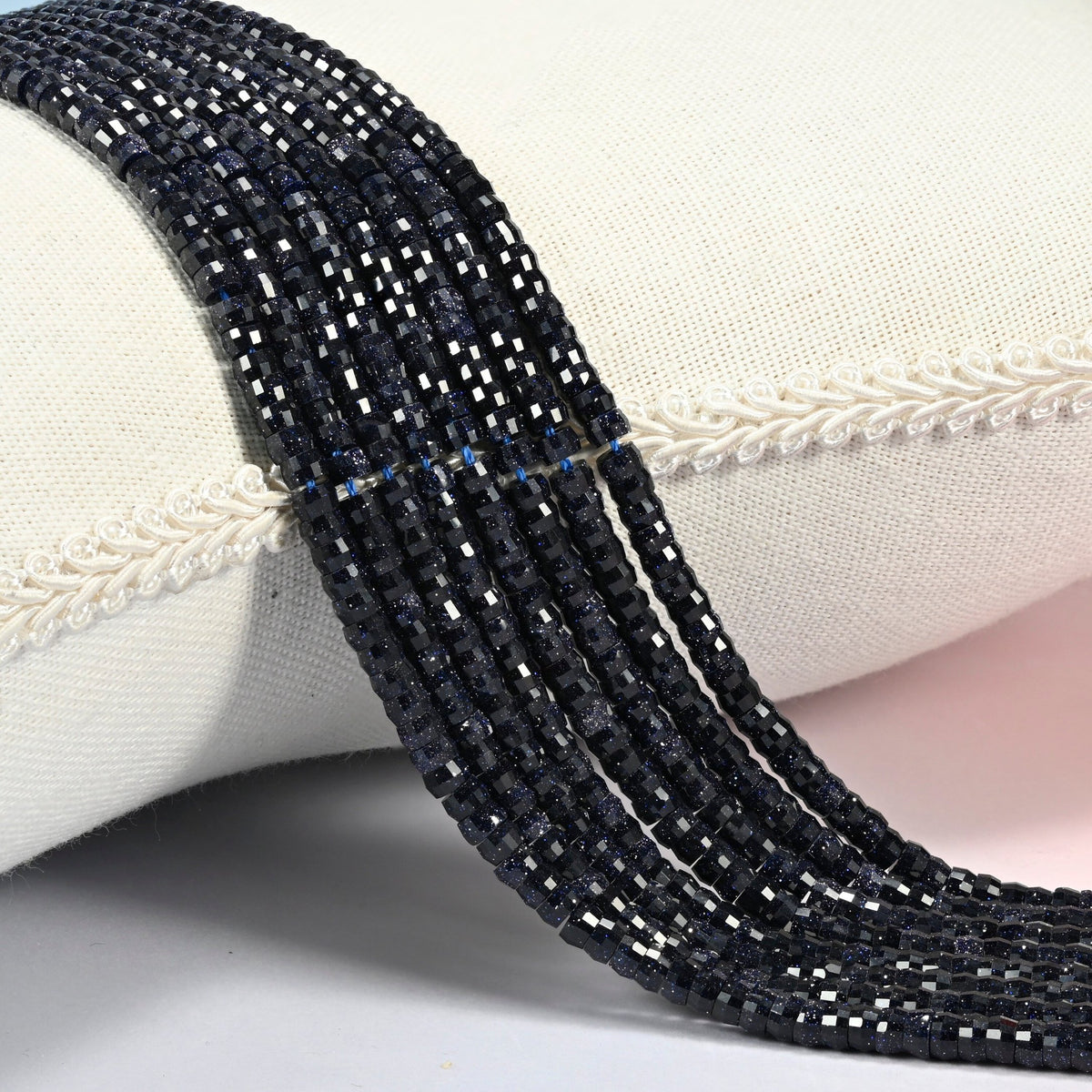 Blue sandstone faceted heishi disc beads 2x4mm, several strands draped over a white cushion