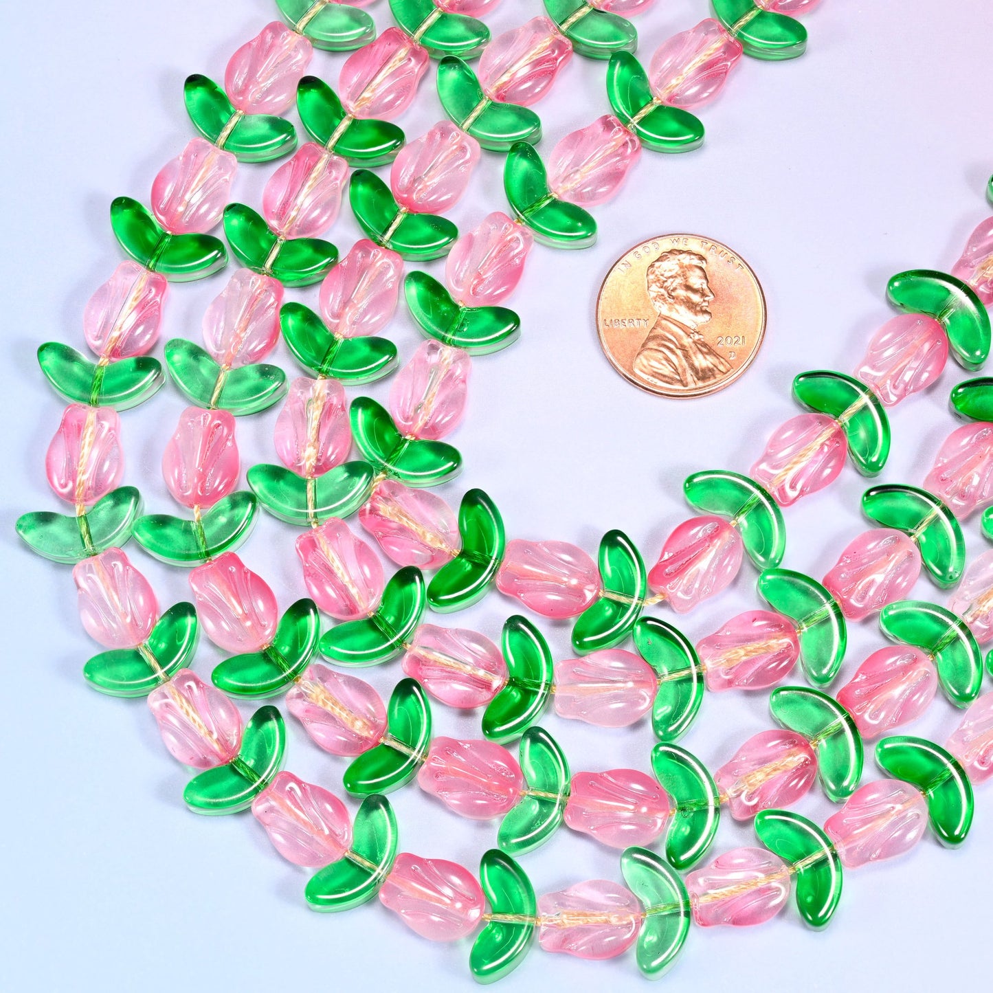 Close-up of pink tulip and green leaf glass beads arranged in a dense coiled cluster on a lavender surface.