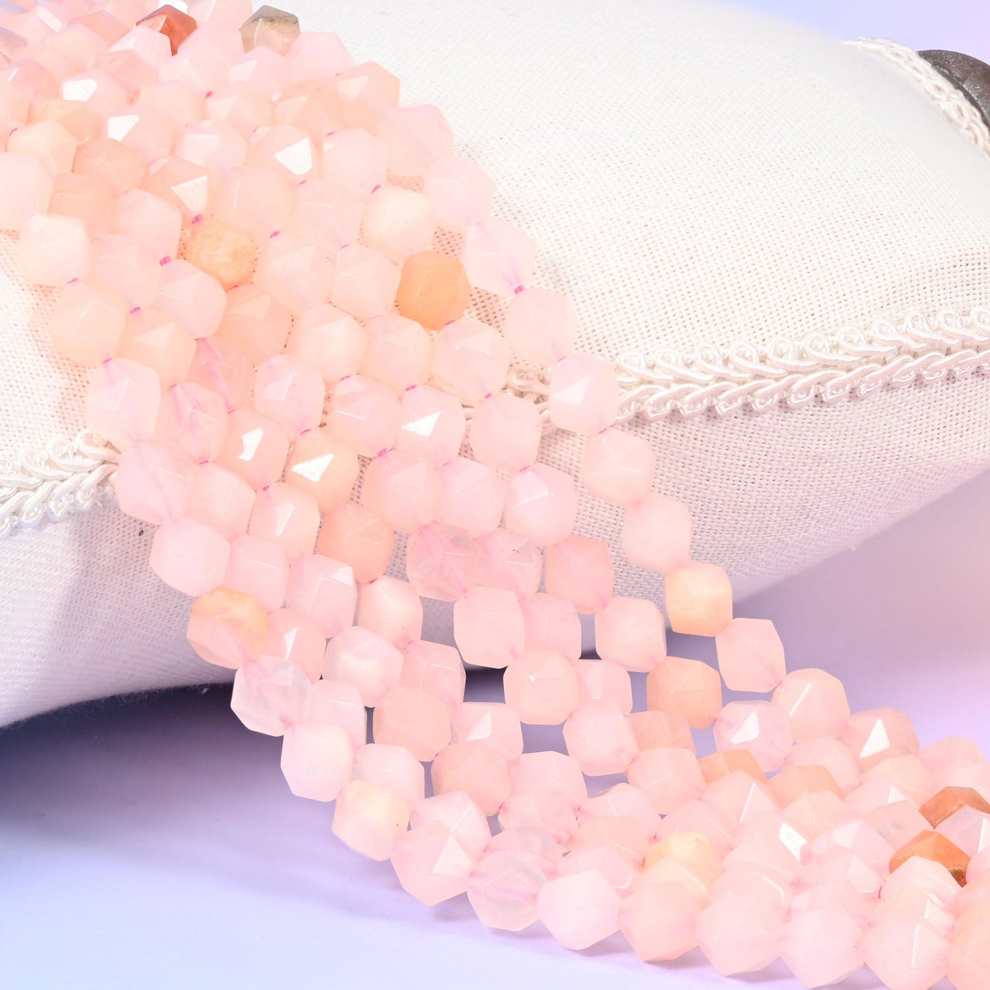 Pink Aventurine diamond star cut beads, strands laid over white fabric, soft blush pink with occasional peach-toned beads