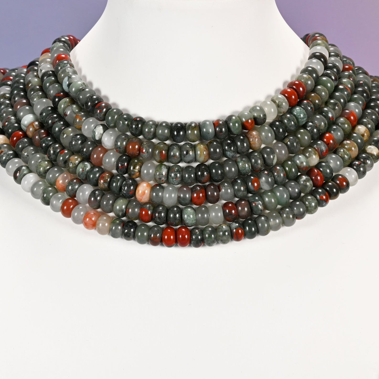 Multi-strand African Bloodstone necklace laid flat on a mannequin neck form against a lavender background.