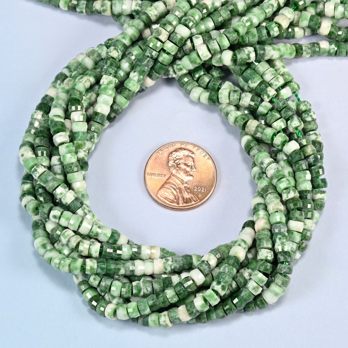 Tree agate faceted heishi disc beads 2x4mm coiled in a loop around a US penny for scale, close-up of the faceted disc shape