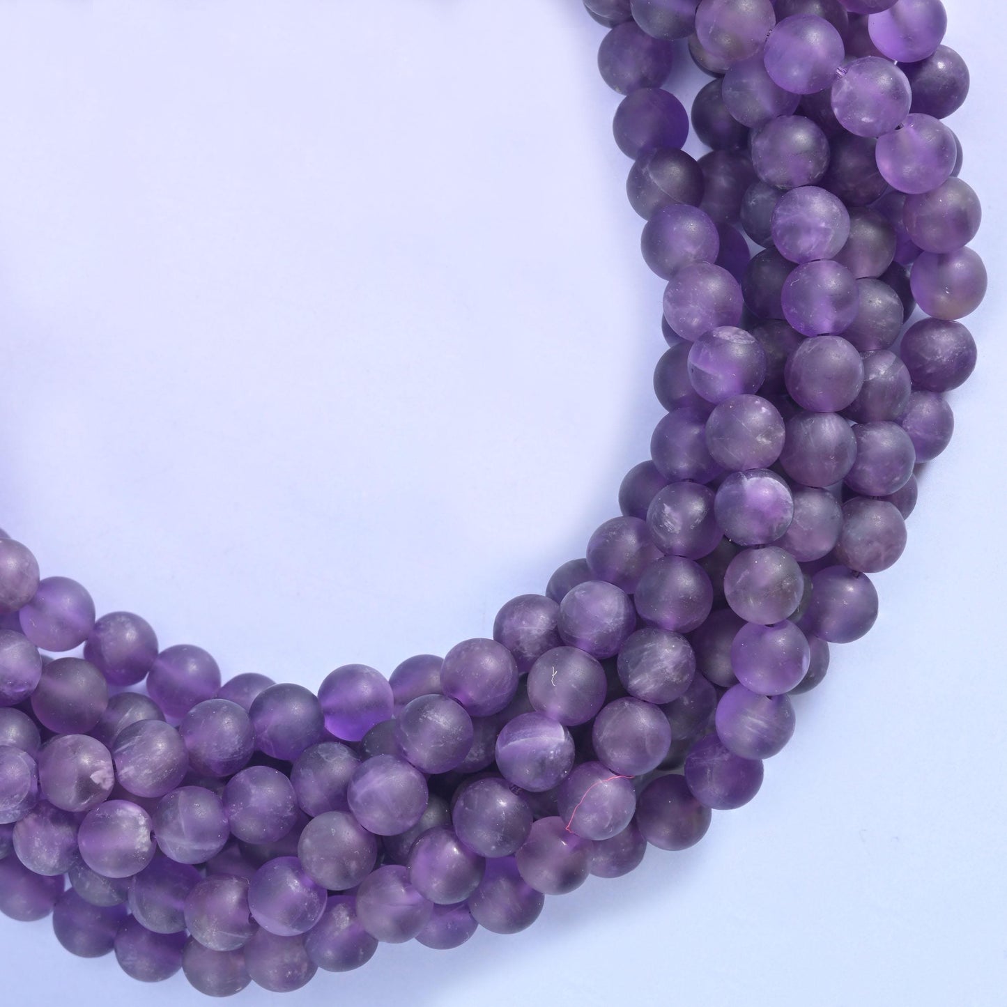 Frosted matte amethyst in medium violet, some beads deeper and smokier, others washed through with pale lavender and grey-white banding