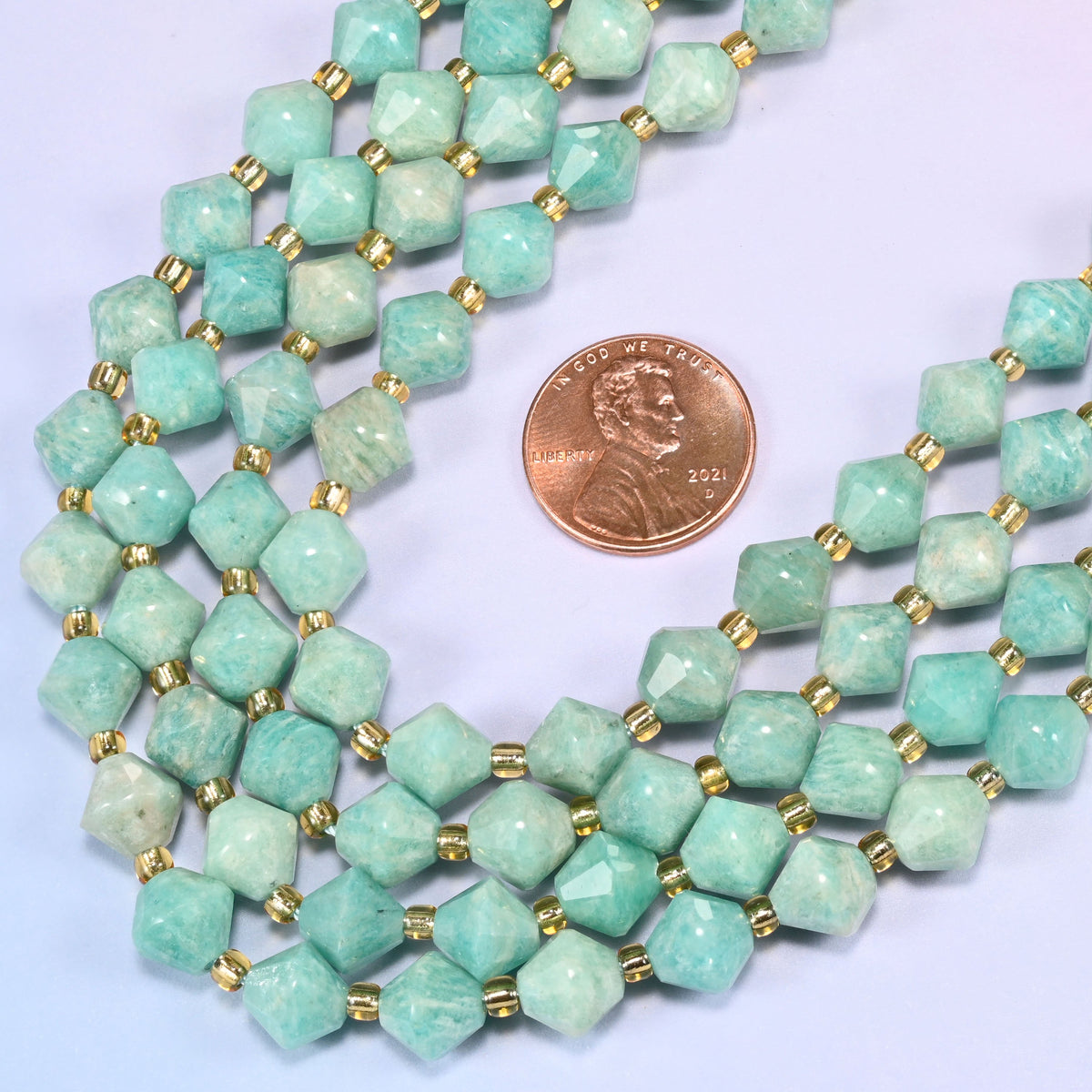 Green Amazonite faceted bicone beads 8mm with gold-tone spacers, strand coiled into a loose loop with a penny alongside for scale