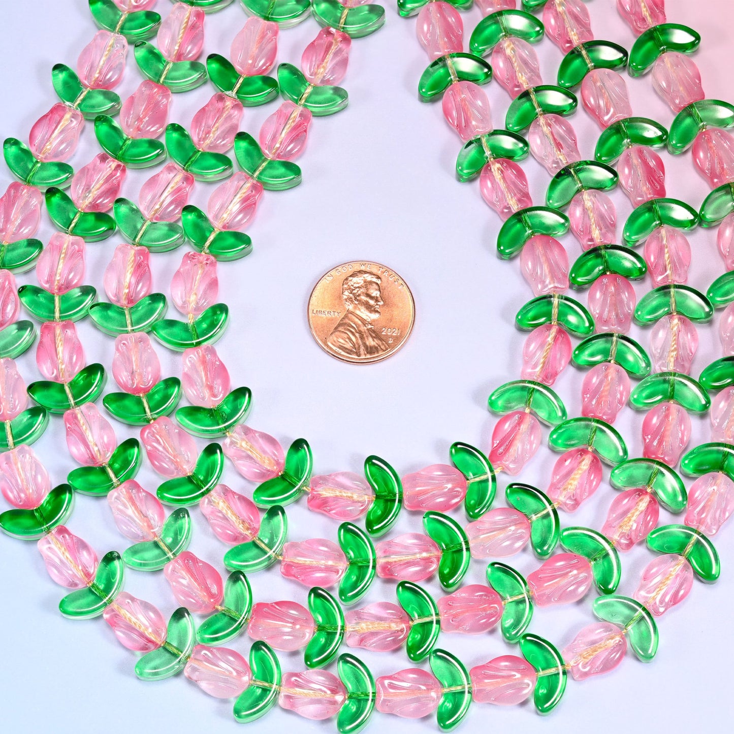 Circular coil of tulip and leaf glass bead strands on a lavender background with a penny in the center for size comparison.