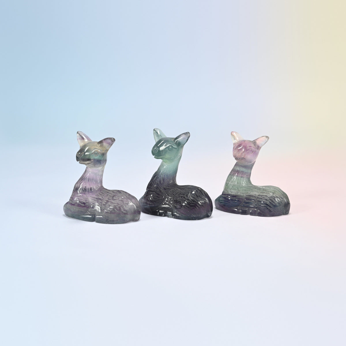 Three rainbow fluorite fawn figurines turned at an angle showing the carved fur lines