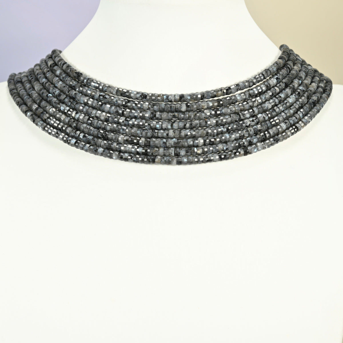 Black labradorite faceted heishi disc strands arranged as a layered collar on a white display bust, dark gray beads across the neck