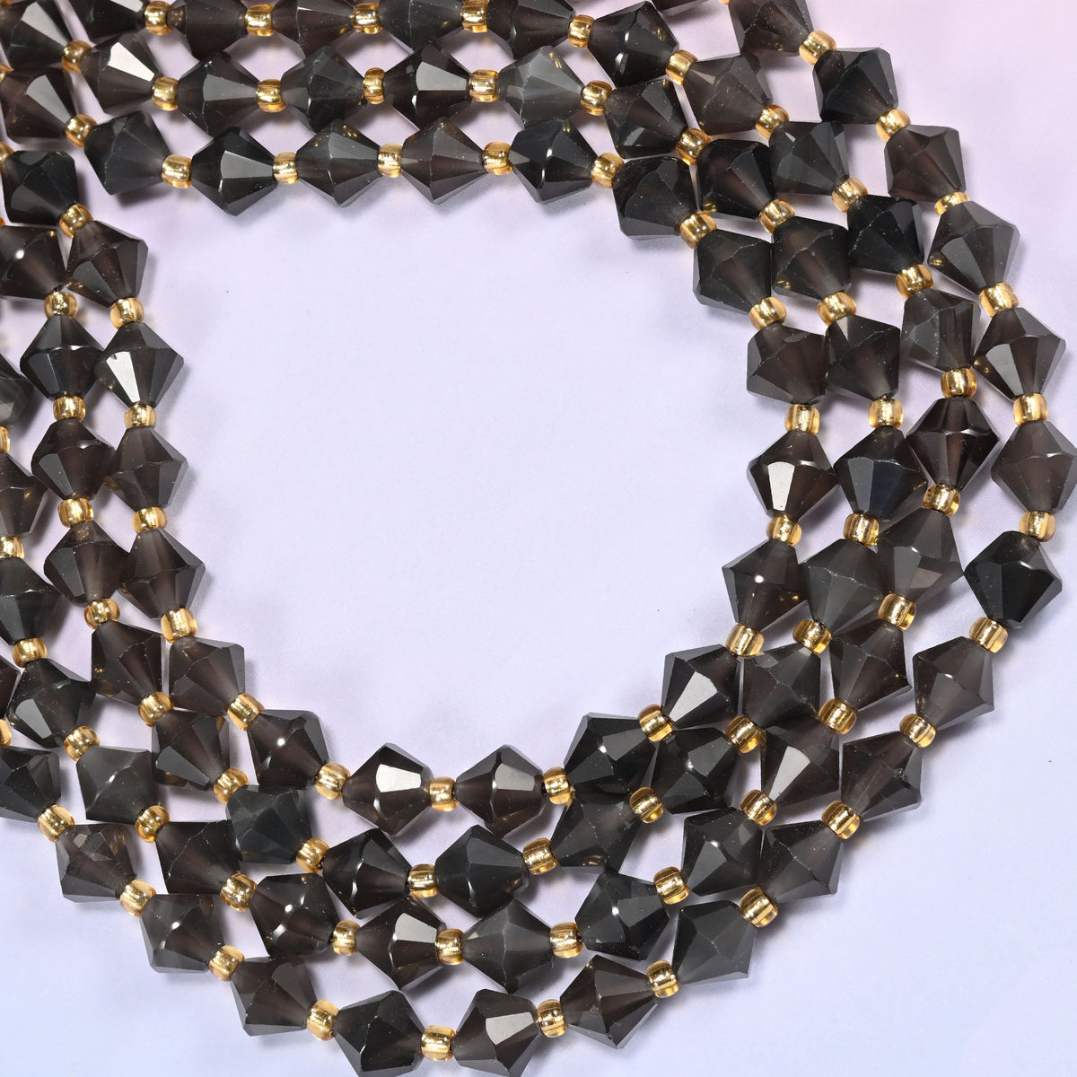 Ice Obsidian faceted bicone beads 8mm with gold-tone spacers, strand coiled into a wide circle, close-up of the faceted texture