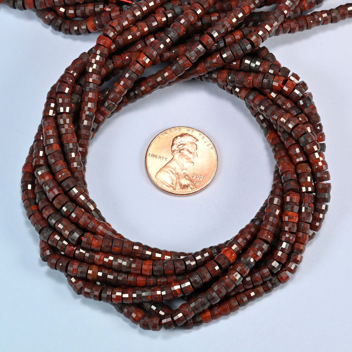 Zhanguo red agate faceted heishi disc beads 2x4mm coiled in a loop around a US penny for scale, close-up of the faceted disc shape