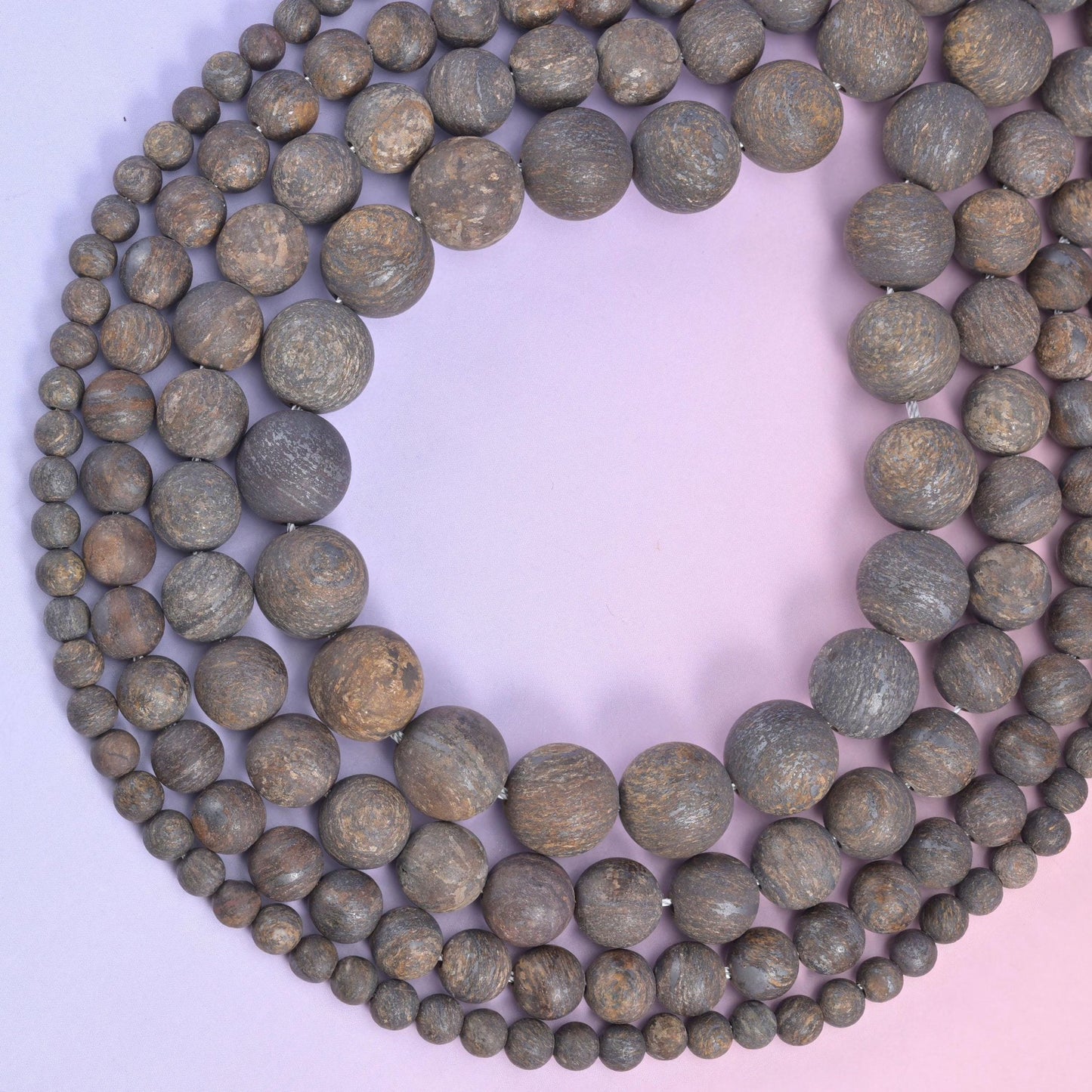 Open loop of mixed-size bronzite rounds on a lilac backdrop, drilled beads strung on cotton cord