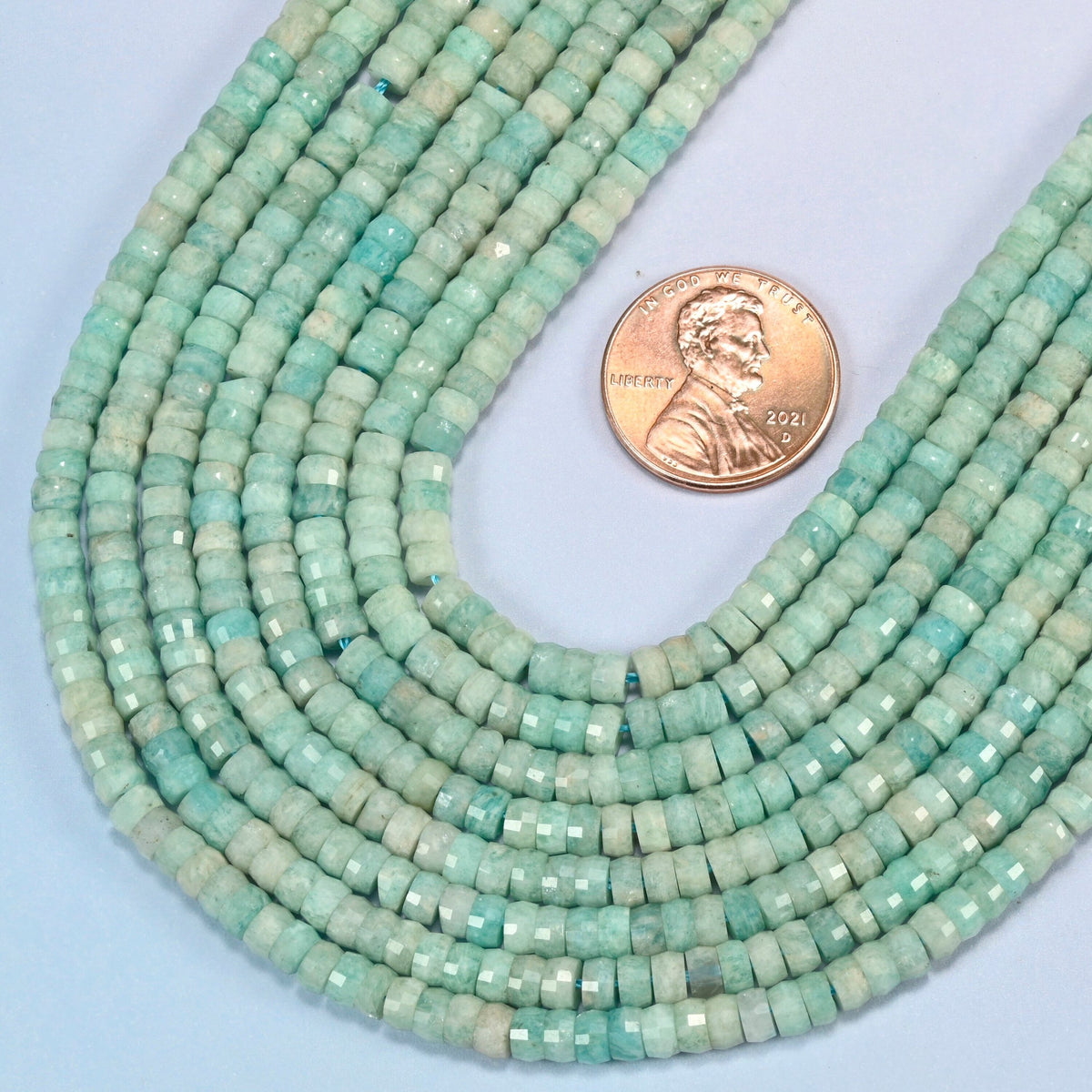 Close view of green amazonite faceted heishi disc strands curving beside a US penny for scale