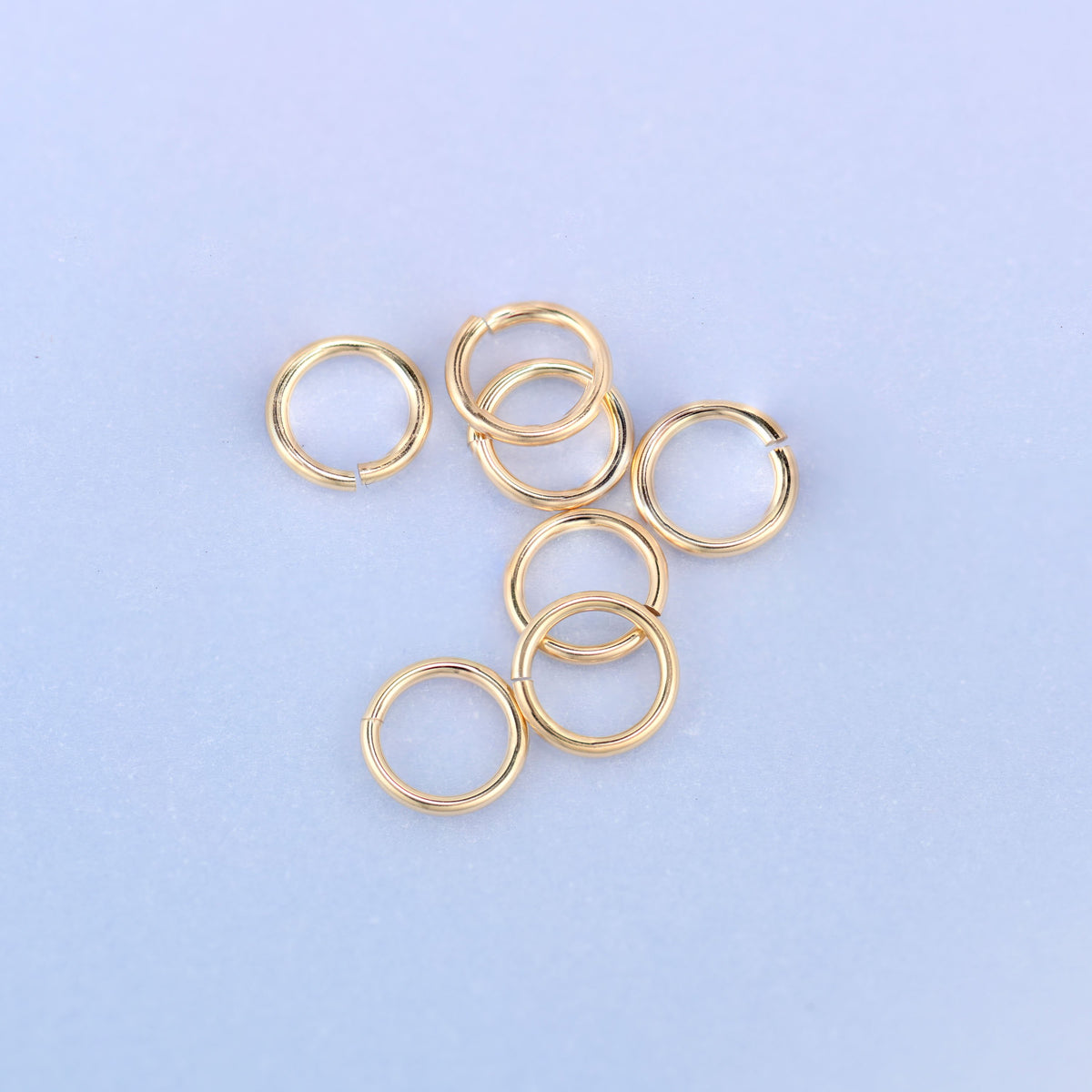 Seven 14K gold filled open jump rings grouped together, some lying flat and one standing on edge, showing the round wire profile and the small split in each ring.